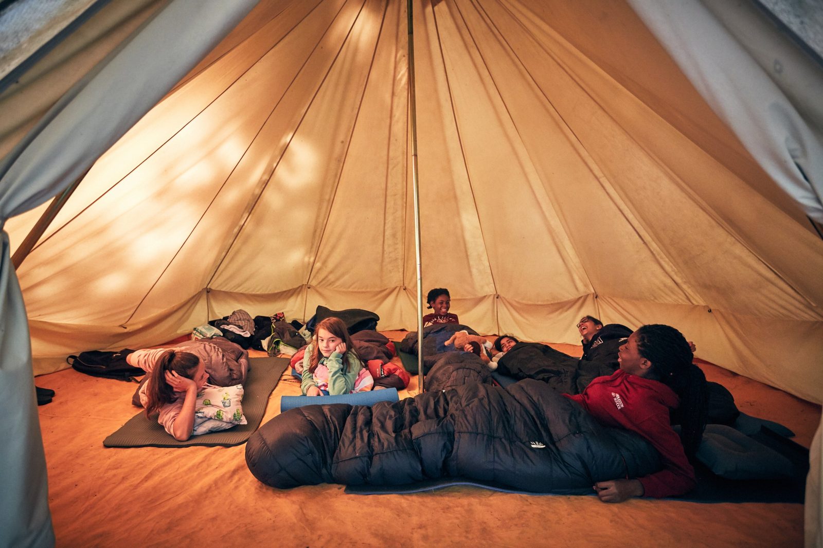 Students relaxing in their sleeping bags inside a cosy bell tent