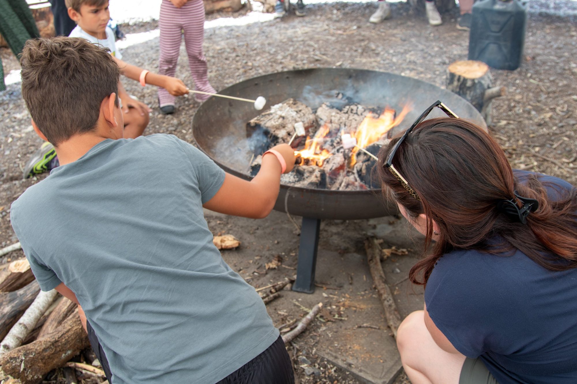 Students toasting marshmallows around the campfire with their teacher on a school residential